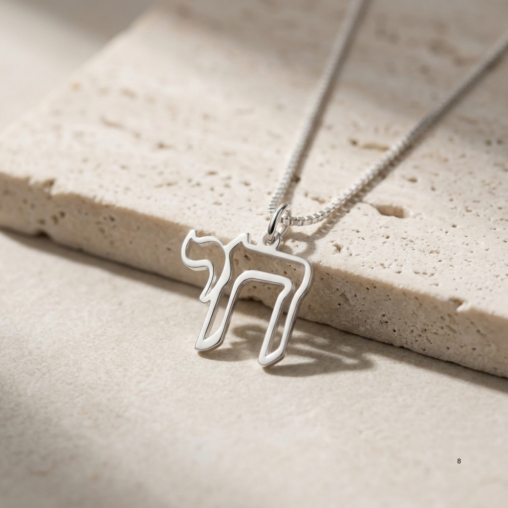 Sterling silver open outline Hebrew Chai pendant resting on light stone