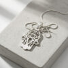 Sterling silver Hamsa evil eye pendant with box chain laid on a grey stone block