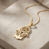 24K gold plated openwork Hamsa pendant with evil eye on a gold chain, lying on stone