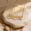 14K yellow gold heart name necklace on a round travertine stone in warm sunlight