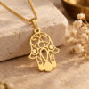14K yellow gold Hamsa pendant with Evil Eye on a box chain, resting on travertine stone beside dried flowers