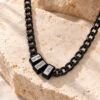 Black Hebrew name necklace for men with engraved name beads on a stainless steel Cuban chain, resting on natural travertine stone