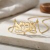 Gold Hebrew name necklace draped on a white stone surface