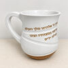 Side view of the white Netilat Yadayim washing cup with the handle on the left, raised gold Hebrew blessing and brown base