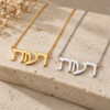 Yellow gold and white gold Hebrew name necklaces lying side by side on travertine stone with dried flowers.