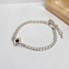 Sterling silver Nano Bible Bracelet lying on a white marble surface beside a stone block, square Tanakh pendant on a Cuban link chain