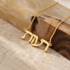 Solid gold Hebrew name necklace draped over olive wood and marble, nameplate reading Reut in classic Hebrew letters.