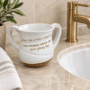 Netilat Yadayim washing cup standing by a bathroom sink with a gold faucet, white polymer natla with gold Hebrew blessing