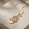14K yellow gold Hamsa pendant with Evil Eye and its chain lying on natural stone