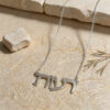 White gold Hebrew name necklace reading Reut on natural stone beside a small rock and a sprig of greenery.