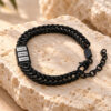 Black Hebrew name bracelet with engraved name beads on natural travertine stone in warm sunlight